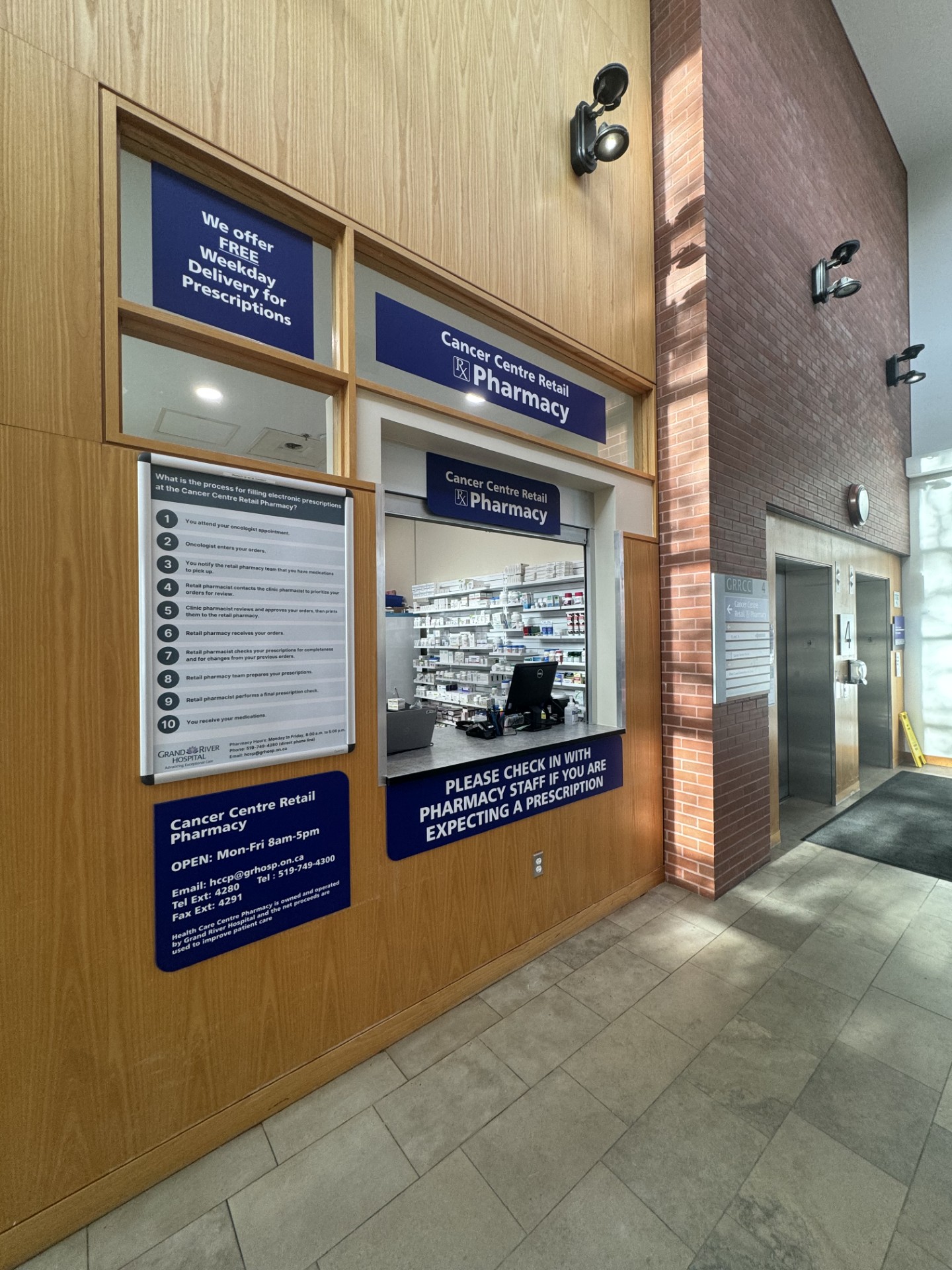 Pharmacy counter with service window, informational signs, and visible shelves of medication in a hospital setting.