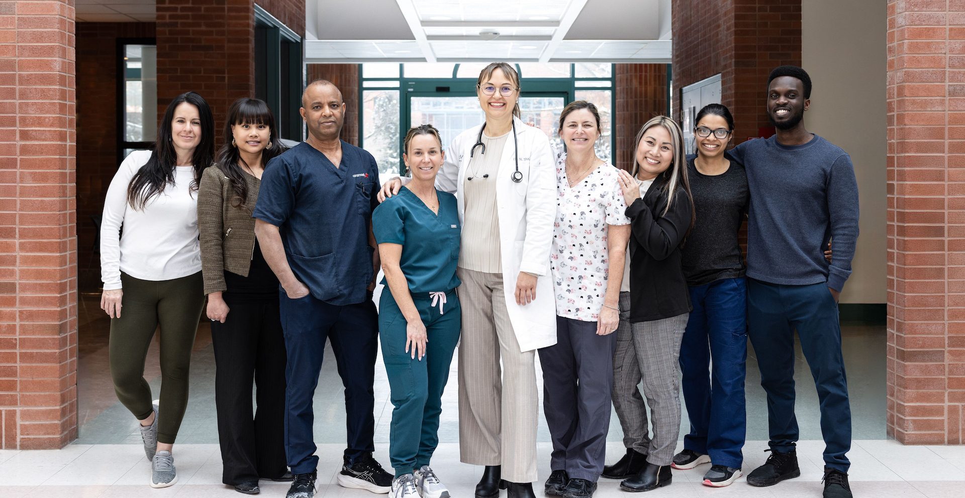 A diverse group of healthcare professionals stands together in a hospital corridor, smiling at the camera.