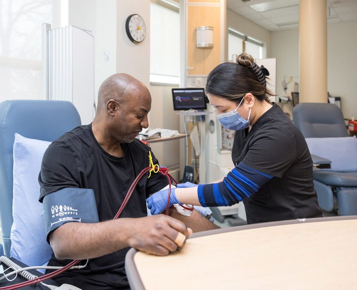 A nurse wearing a mask draws blood from a seated patient’s arm in a medical clinic.