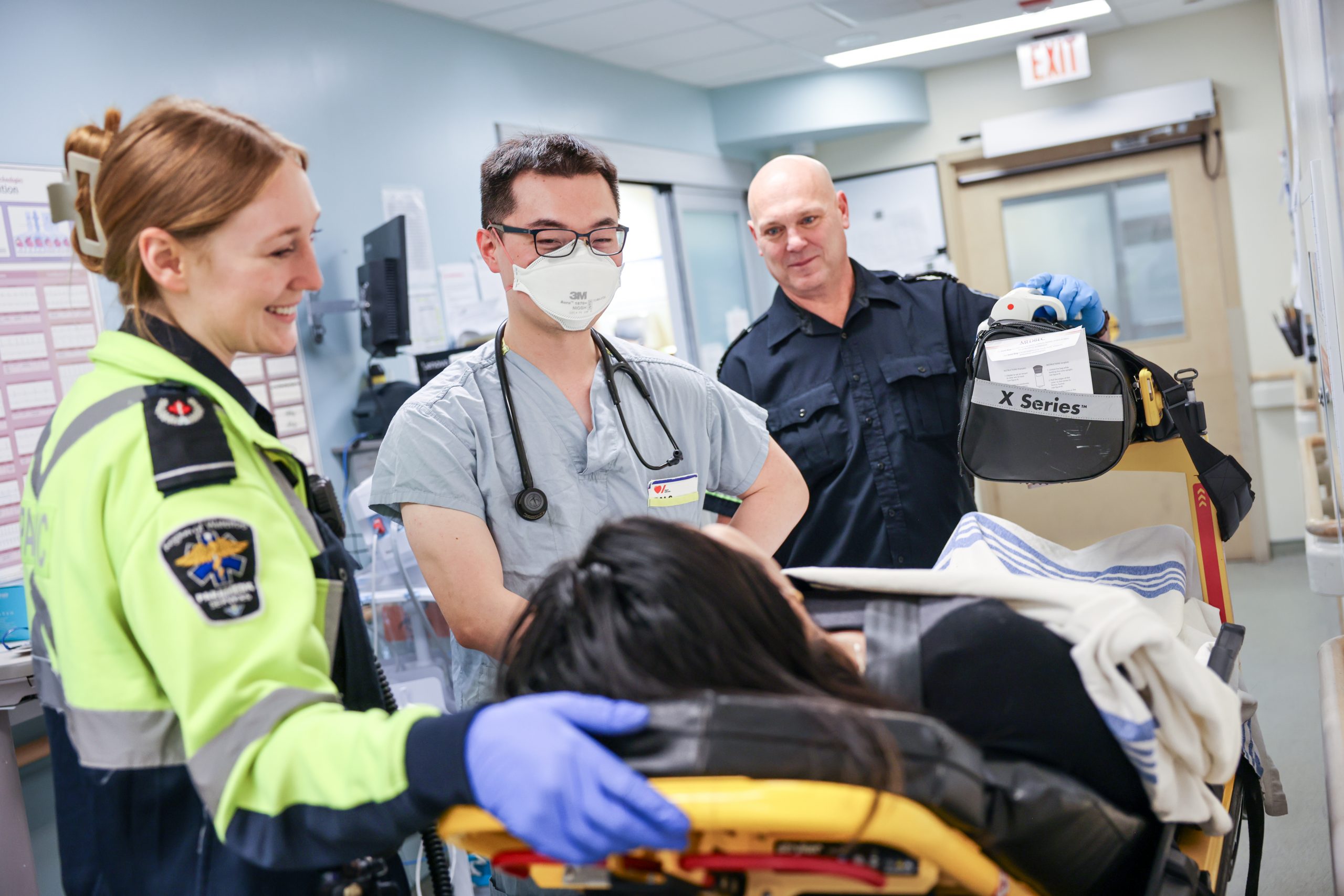 Medical staff and paramedics attend to a patient on a stretcher in a hospital corridor.
