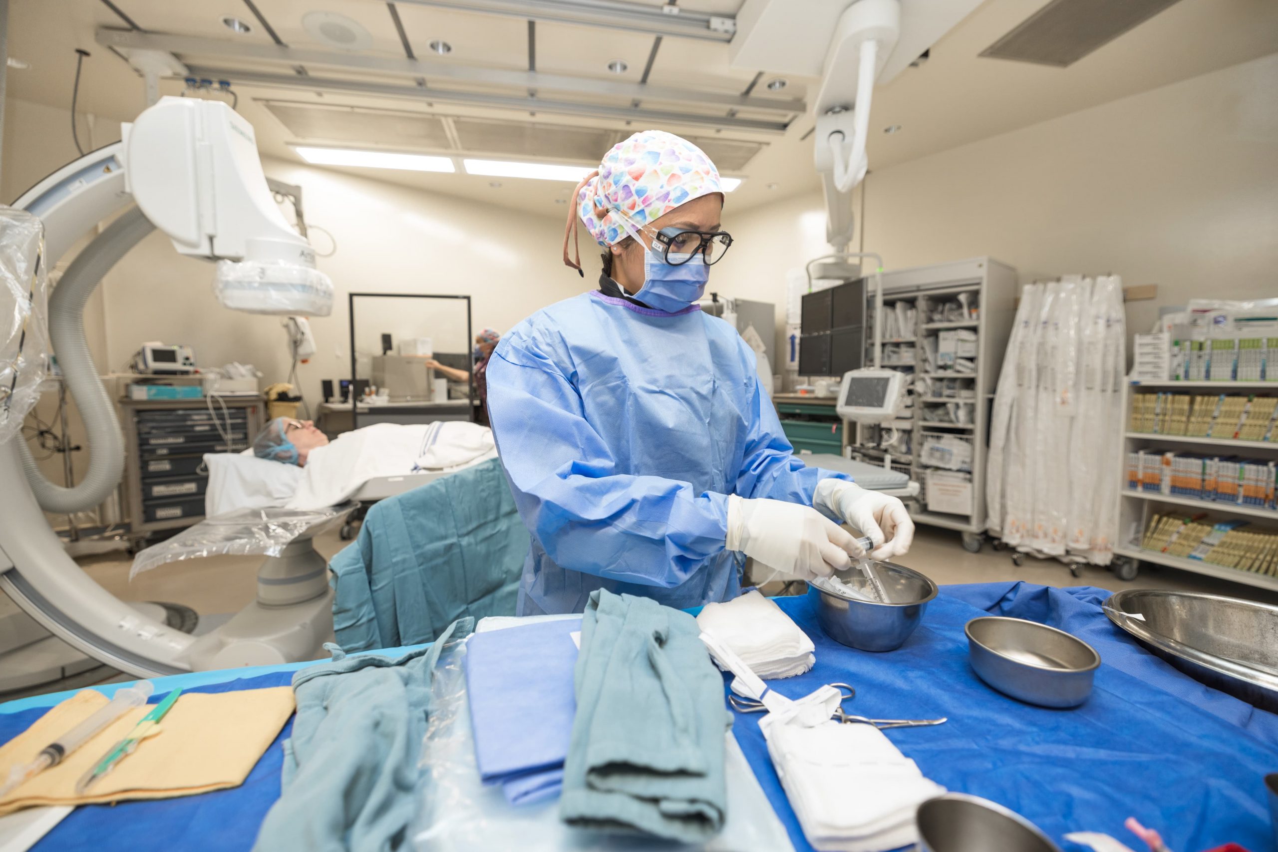 A medical professional in scrubs prepares surgical instruments in a hospital operating room.