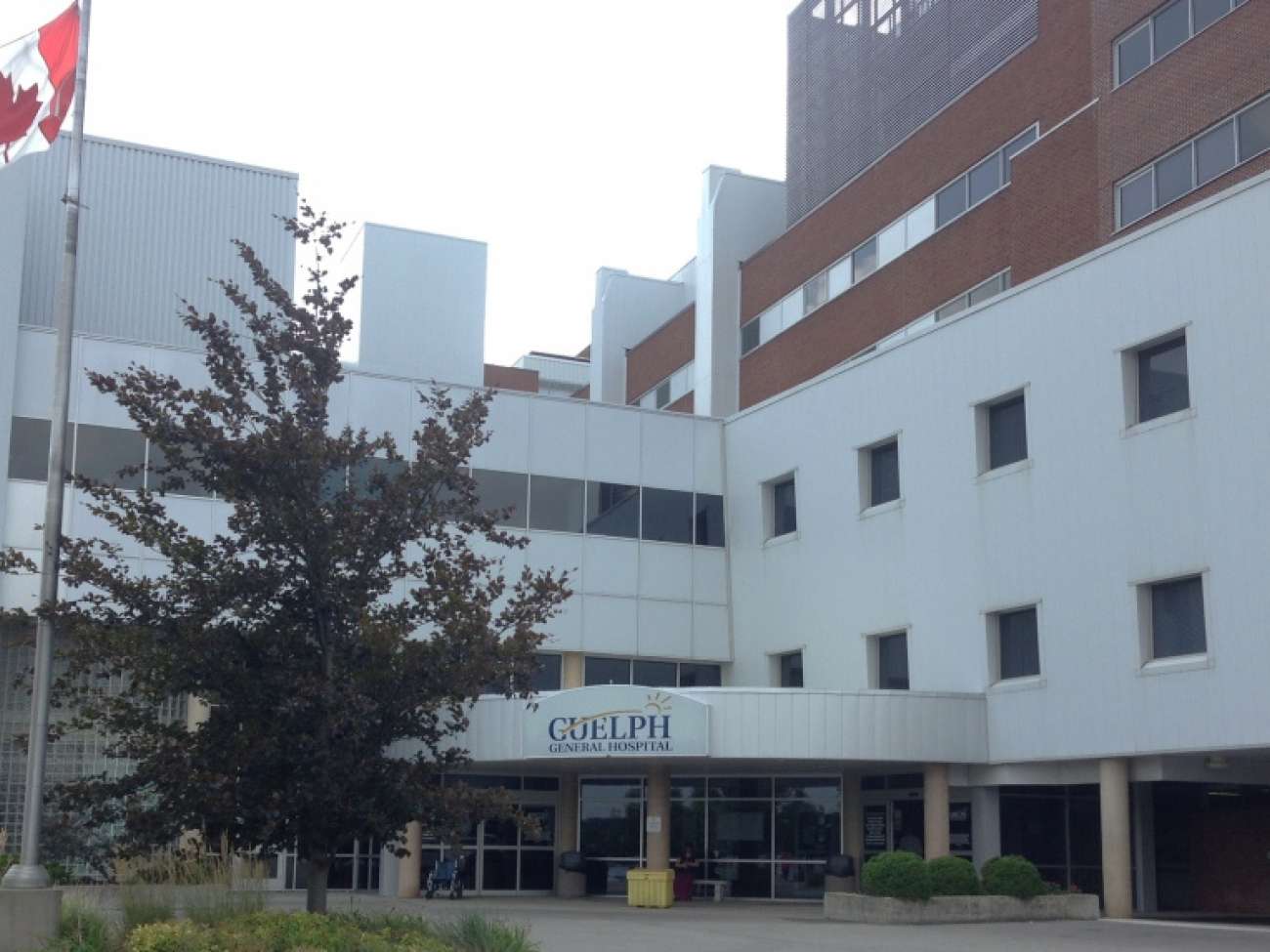 The entrance of Guelph General Hospital with a Canadian flag and trees in front of the building.