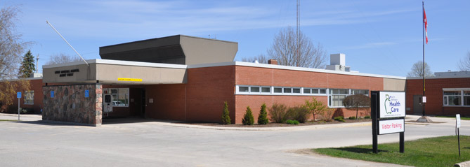 Single-story brick building with a flat roof, labeled as a health care center, with a visitor parking sign in front.