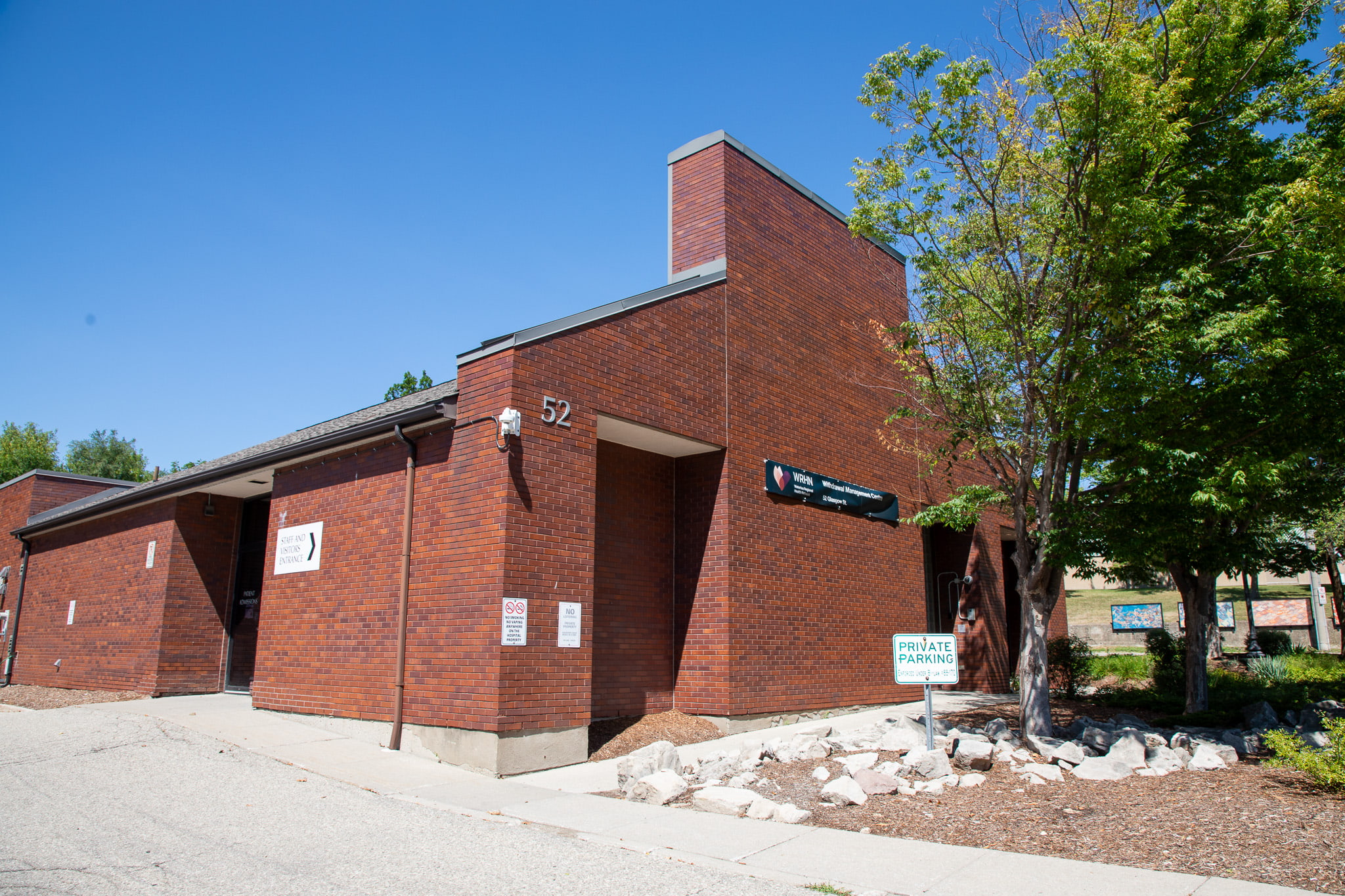 A brick building with the number 52 and signs for private parking and directory information on a sunny day.