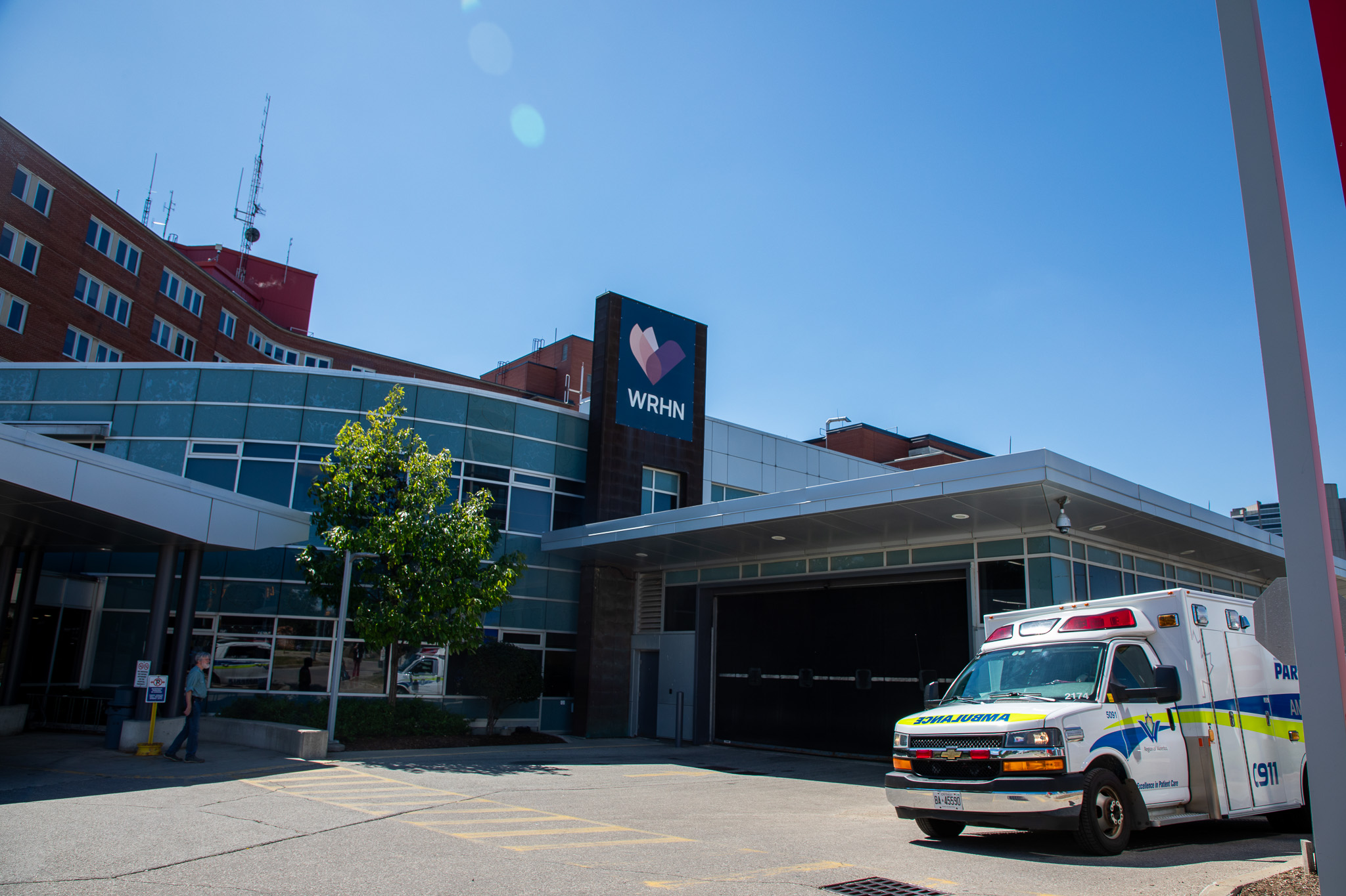 An ambulance is parked outside the entrance of a hospital with a WHRN sign on a sunny day.
