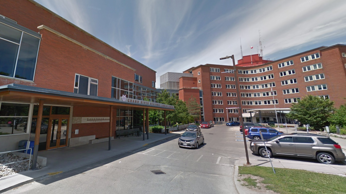 A brick hospital building with an entrance canopy, parked cars, and a partly cloudy sky overhead.